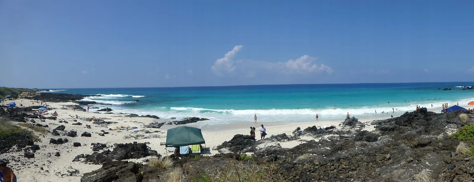Panoramablick auf einen weißen Sandstrand in Hawaii mit türkisblauem Wasser, Felsen und Strandbesuchern