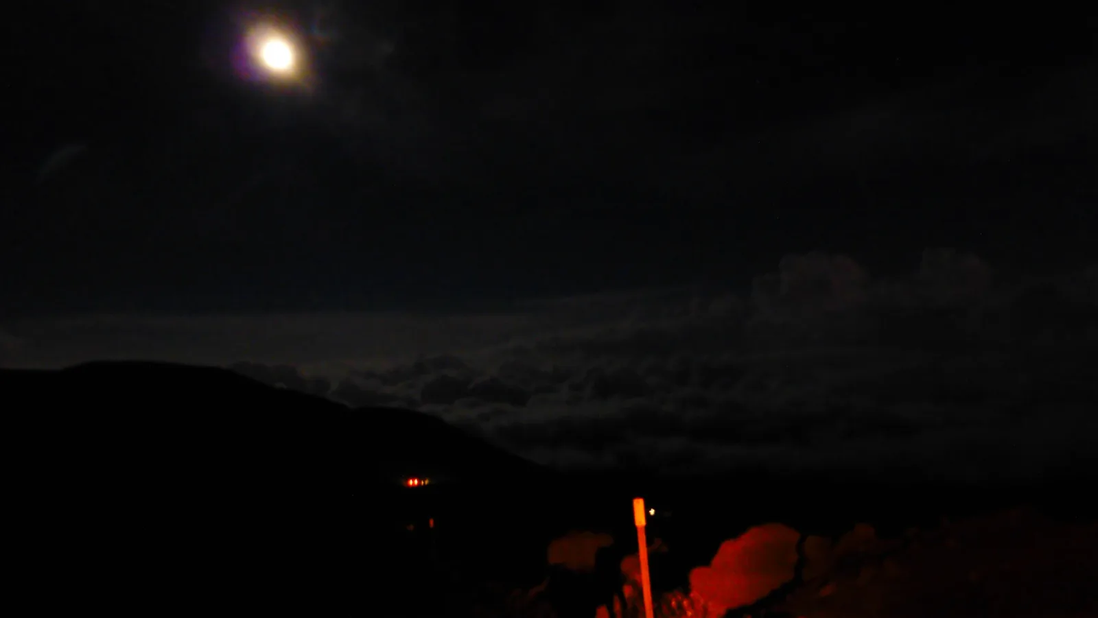 Vollmond erhellt nächtlichen Himmel über dunkler Vulkanlandschaft auf Hawaii mit Lagerfeuer