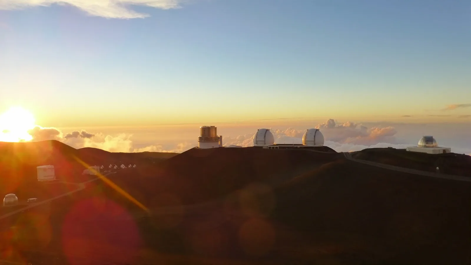 Teleskop-Observatorien auf dem Gipfel des Mauna Kea über einer Wolkendecke bei goldenem Sonnenuntergang